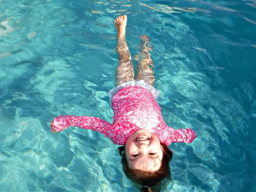 A girl in a pink rash guard floating on her back in a pool