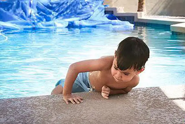 A boy pulling himself up onto the edge of a pool