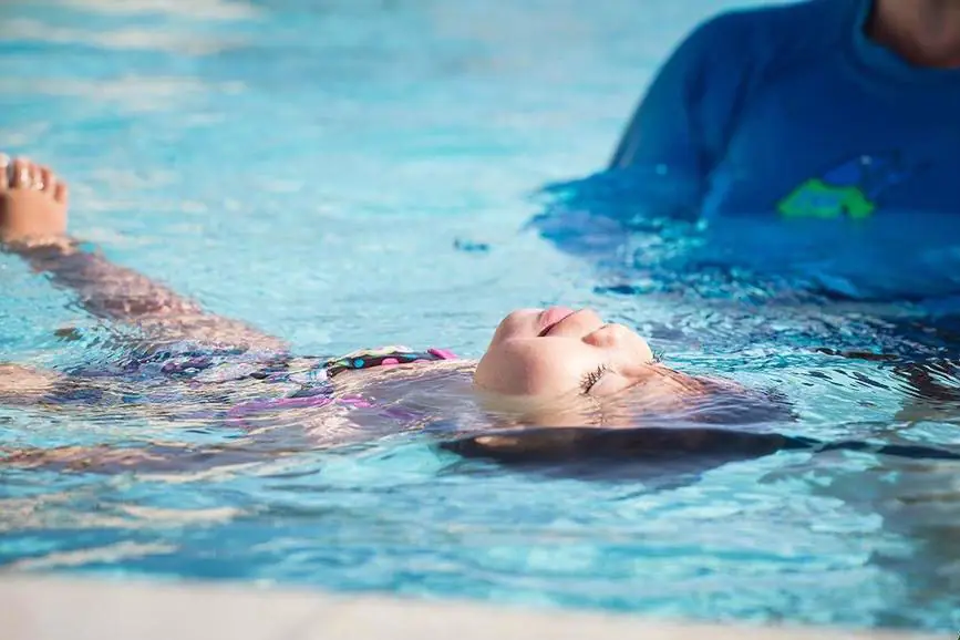 An infant floating face up on the surface of a pool, eyes half closed