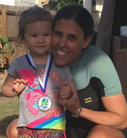 Glare Sanchez smiling beside a toddler who is wearing a swim medal