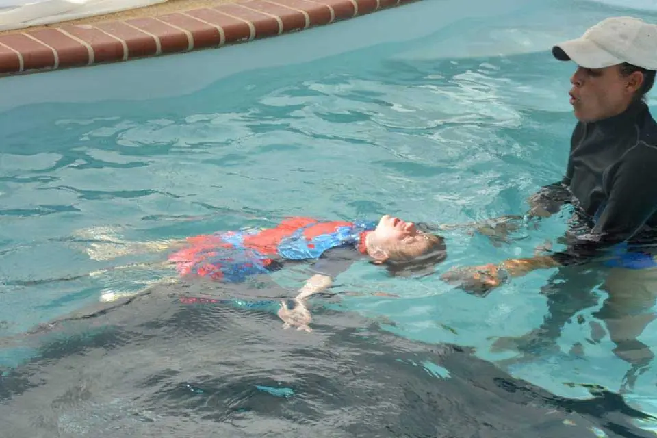 An ISR instructor standing in a pool beside a child floating on her back